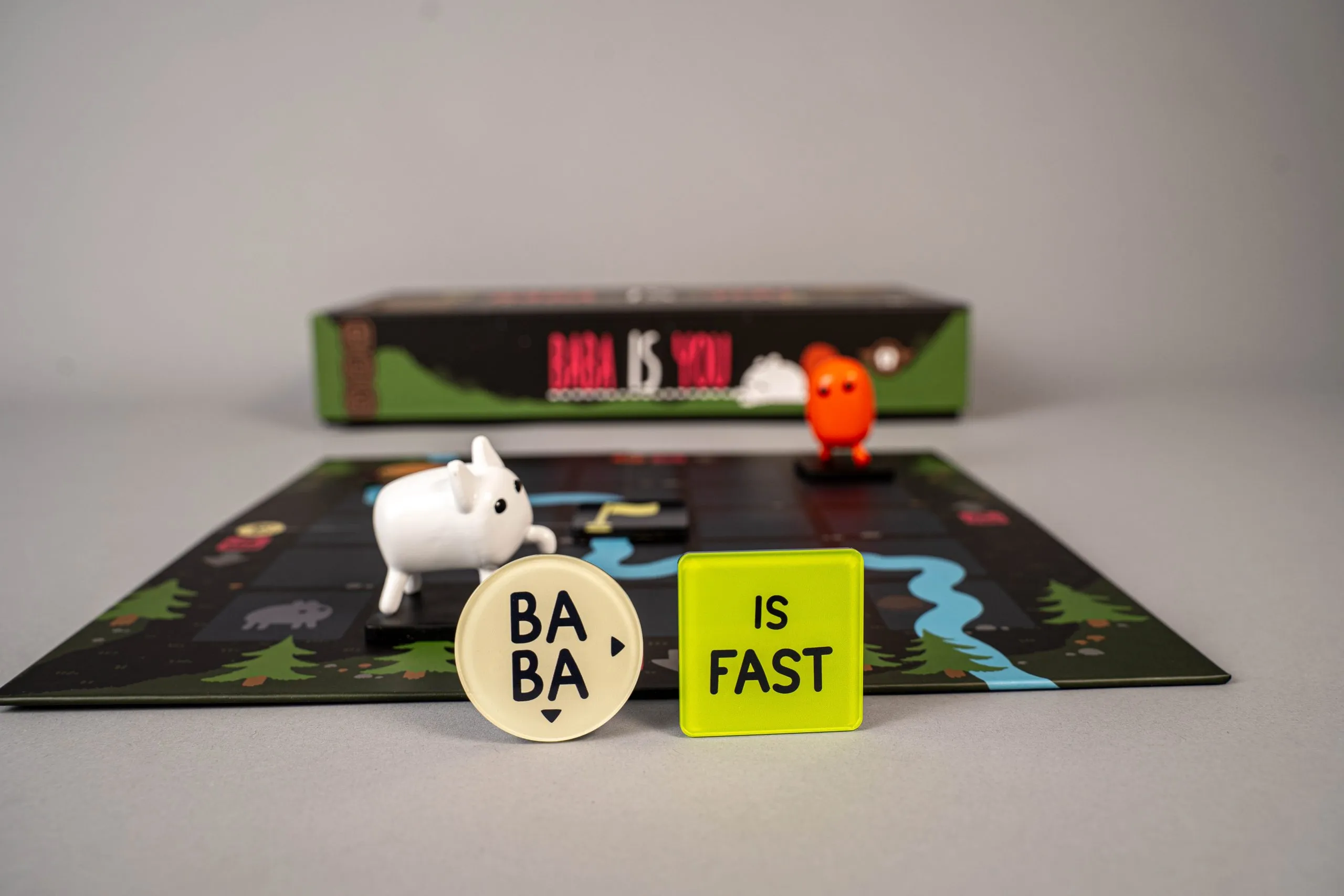 Baba and Keke figures on a physical board beside BABA and IS FAST rule tokens.