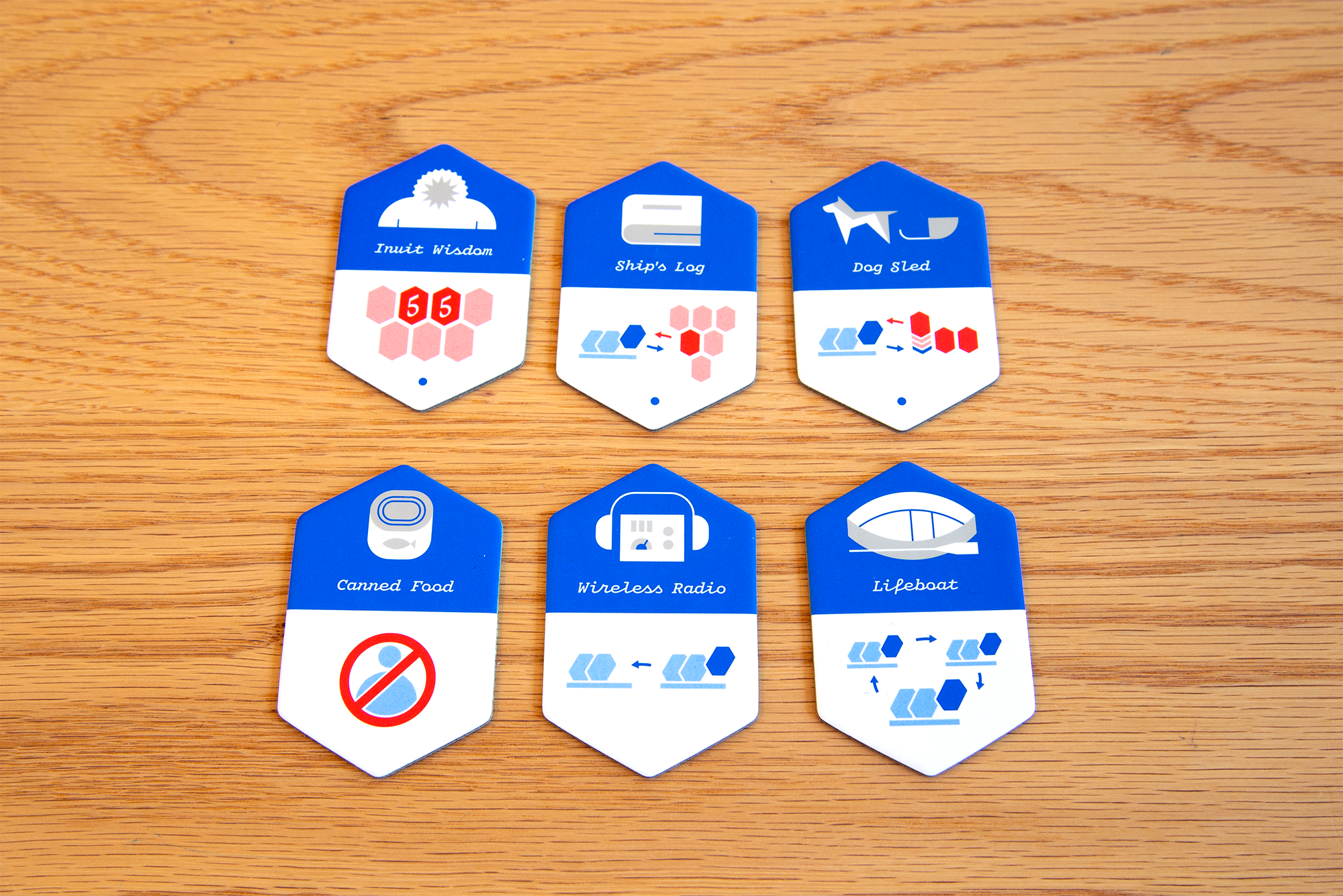 Six blue item chips including Wireless Radio, Dog Sled and Lifeboat on a wooden table.