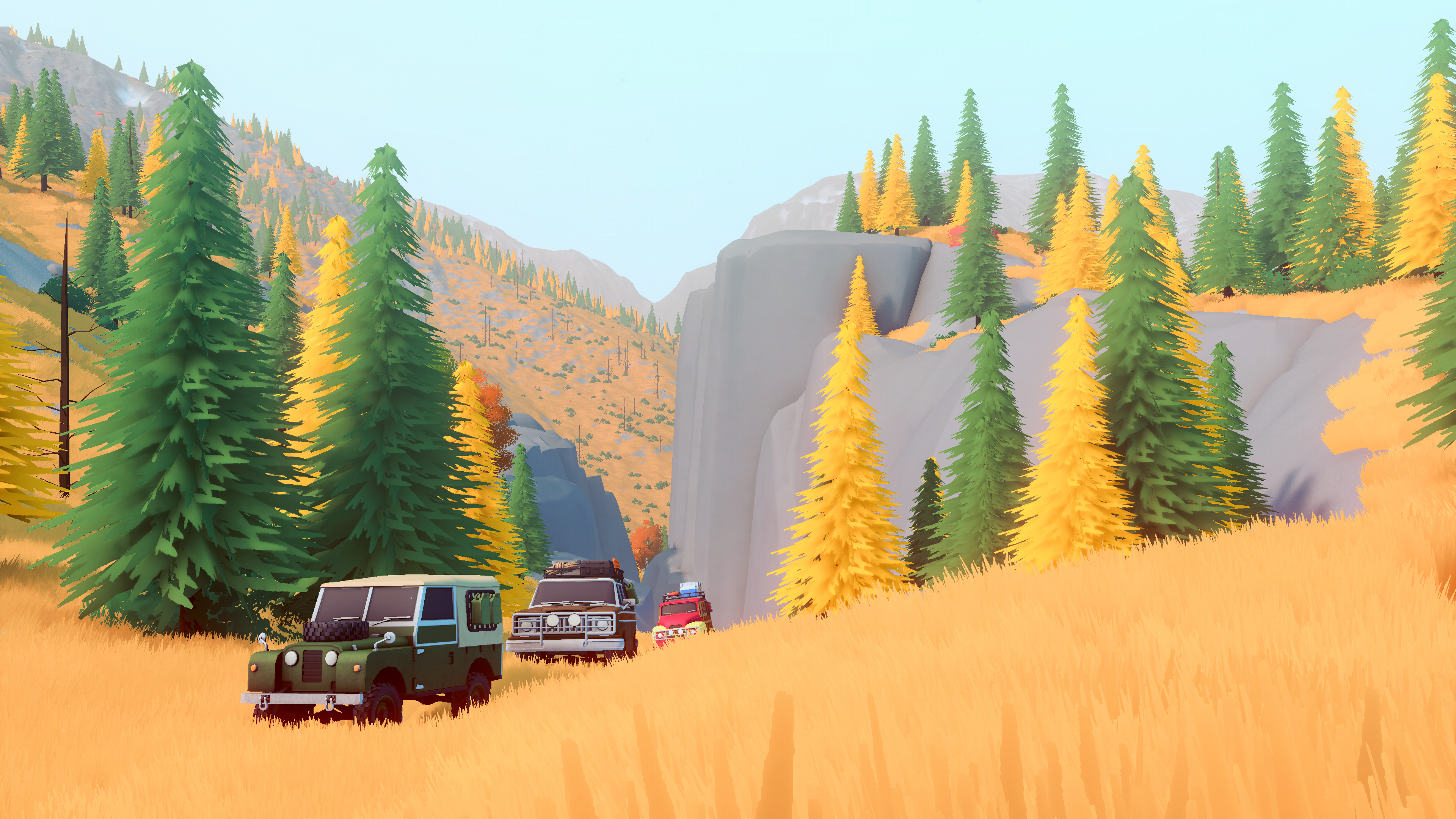 Three off-road vehicles cross golden grass below conifers and tall grey cliffs.