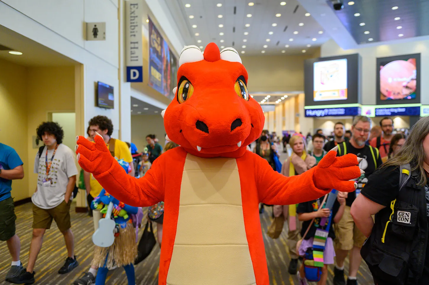 Official Gen Con photo showing the convention mascot greeting attendees in a busy Indianapolis convention corridor.