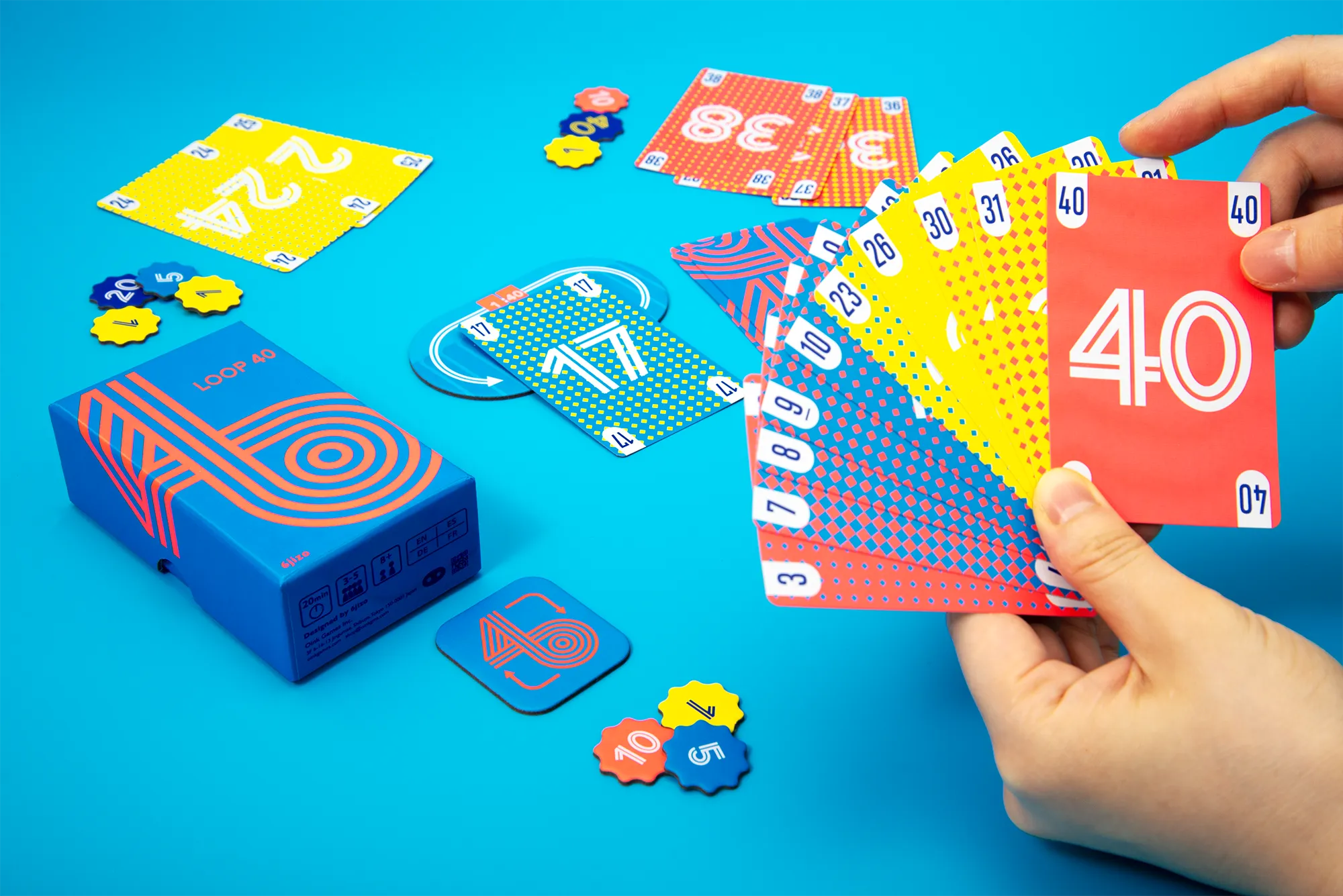 Official Loop 40 press photograph showing a hand of numbered cards, the box and tokens on a turquoise table.