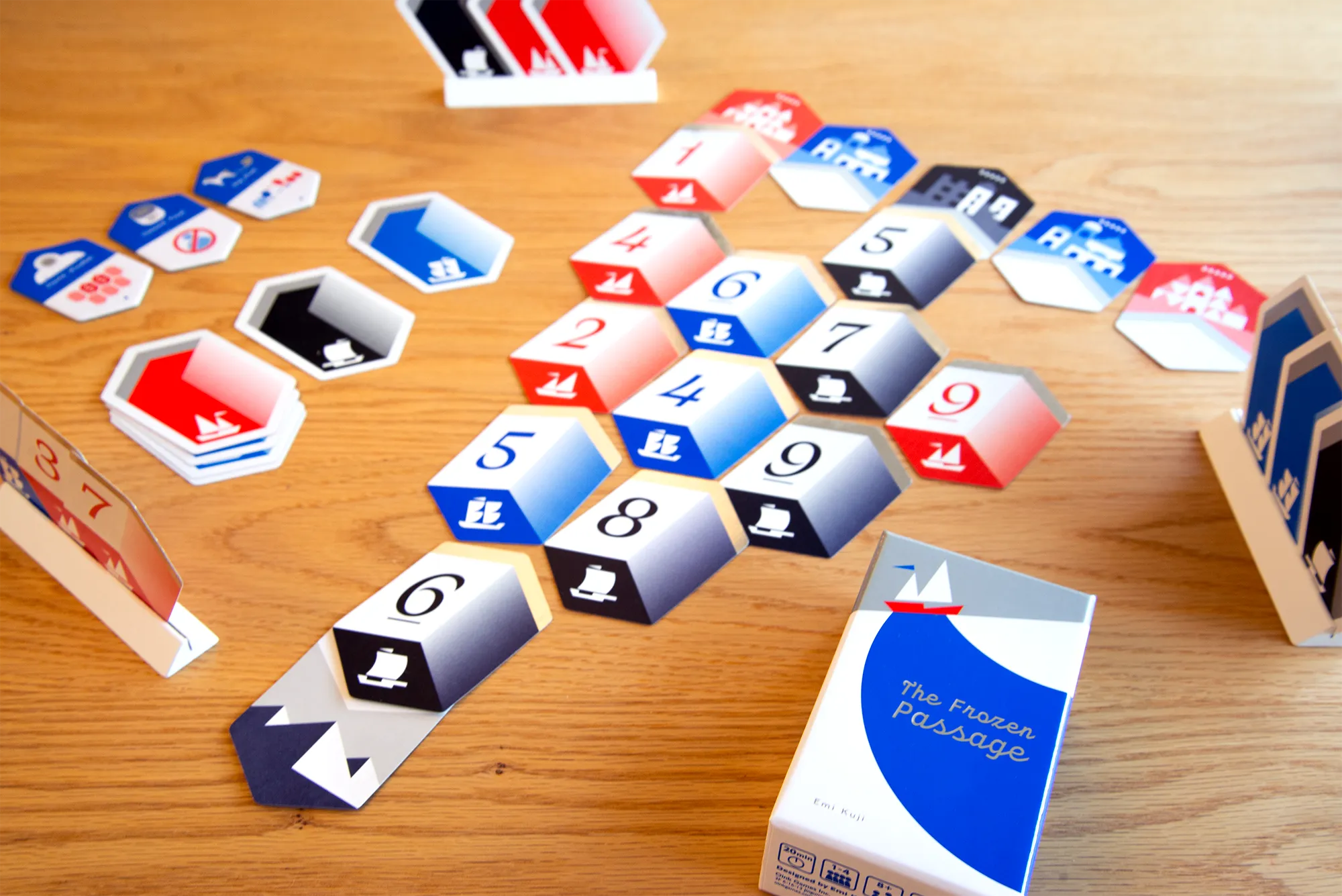 The Frozen Passage numbered cards form a route on a wooden table beside card stands and the box.