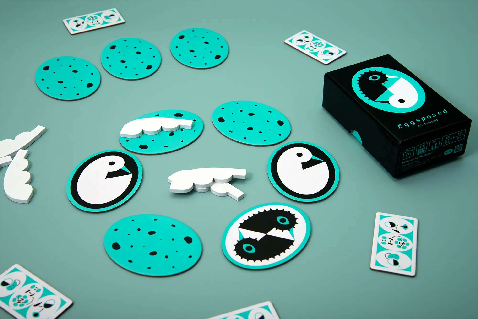 Official Oink Games press photograph of the Eggsposed box, bird egg tiles, role cards and white wooden feather markers.