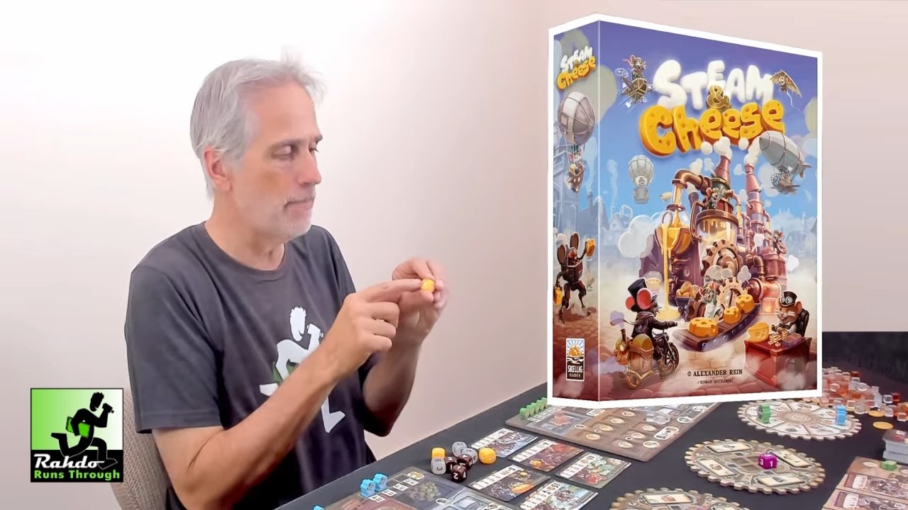 Still from Rahdo Runs Through' Steam & Cheese preview, showing the game’s illustrated factory board and components.