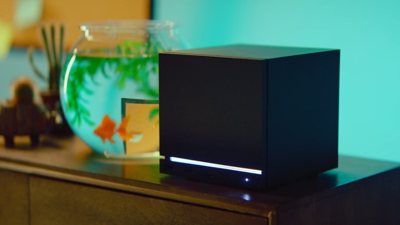 Official Valve Steam Machine lifestyle image showing the black system on a table beside a fishbowl in a home setup.