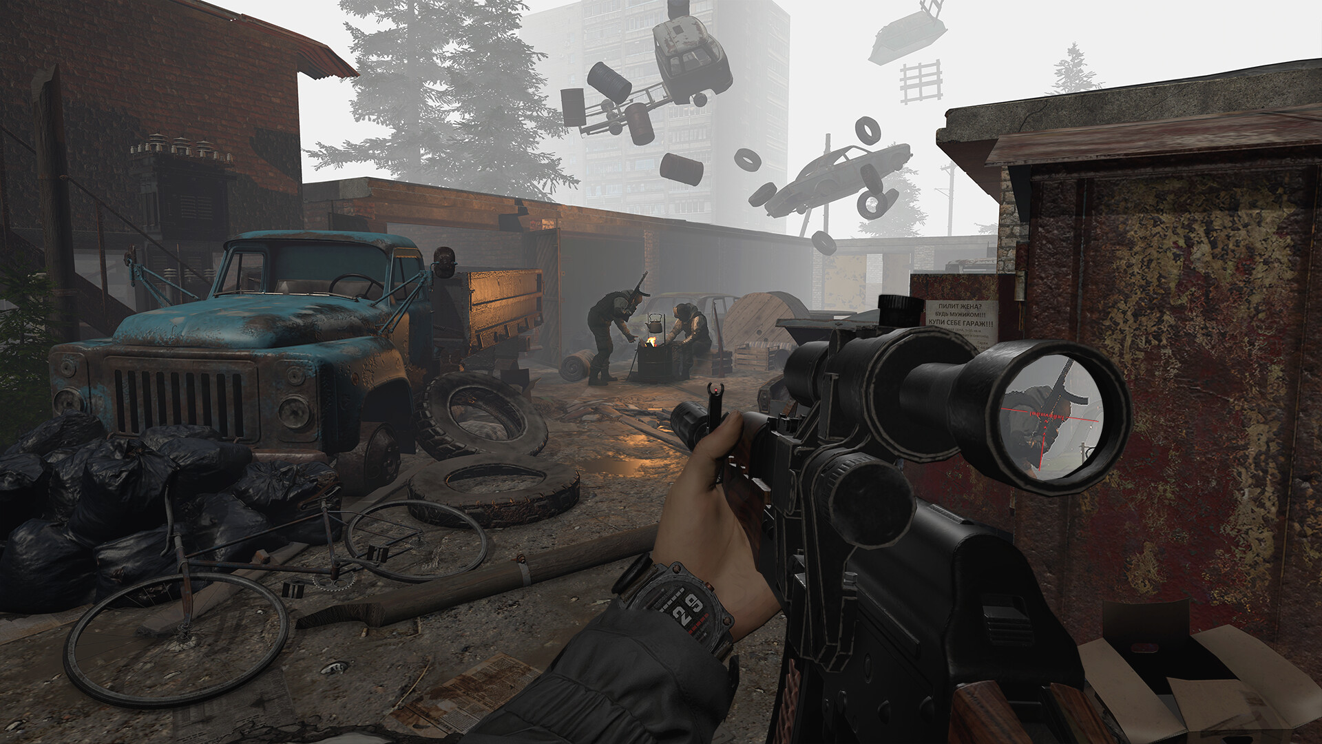 Armed figures beside a fire in an industrial yard beneath floating vehicles and debris.