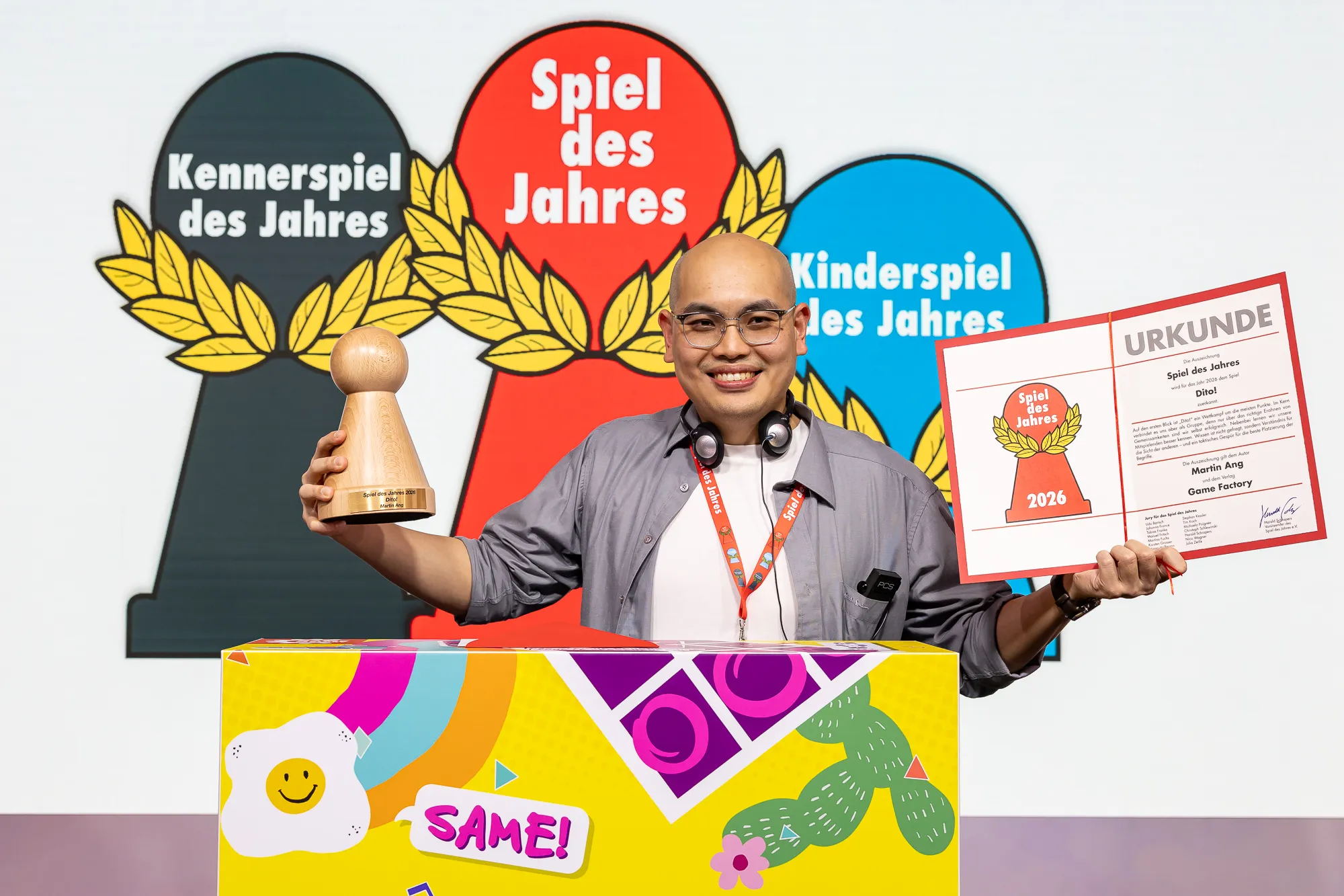 Dito designer Martin Ang holds his 2026 award and certificate behind a colourful game display.